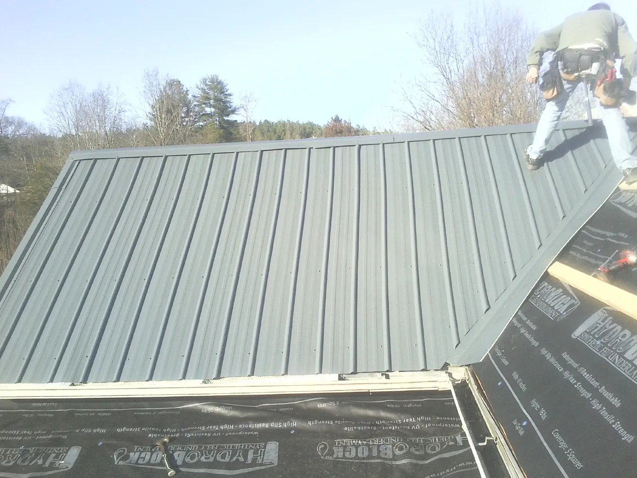 Crew installing dark green standing seam panels over synthetic underlayment in Bedford