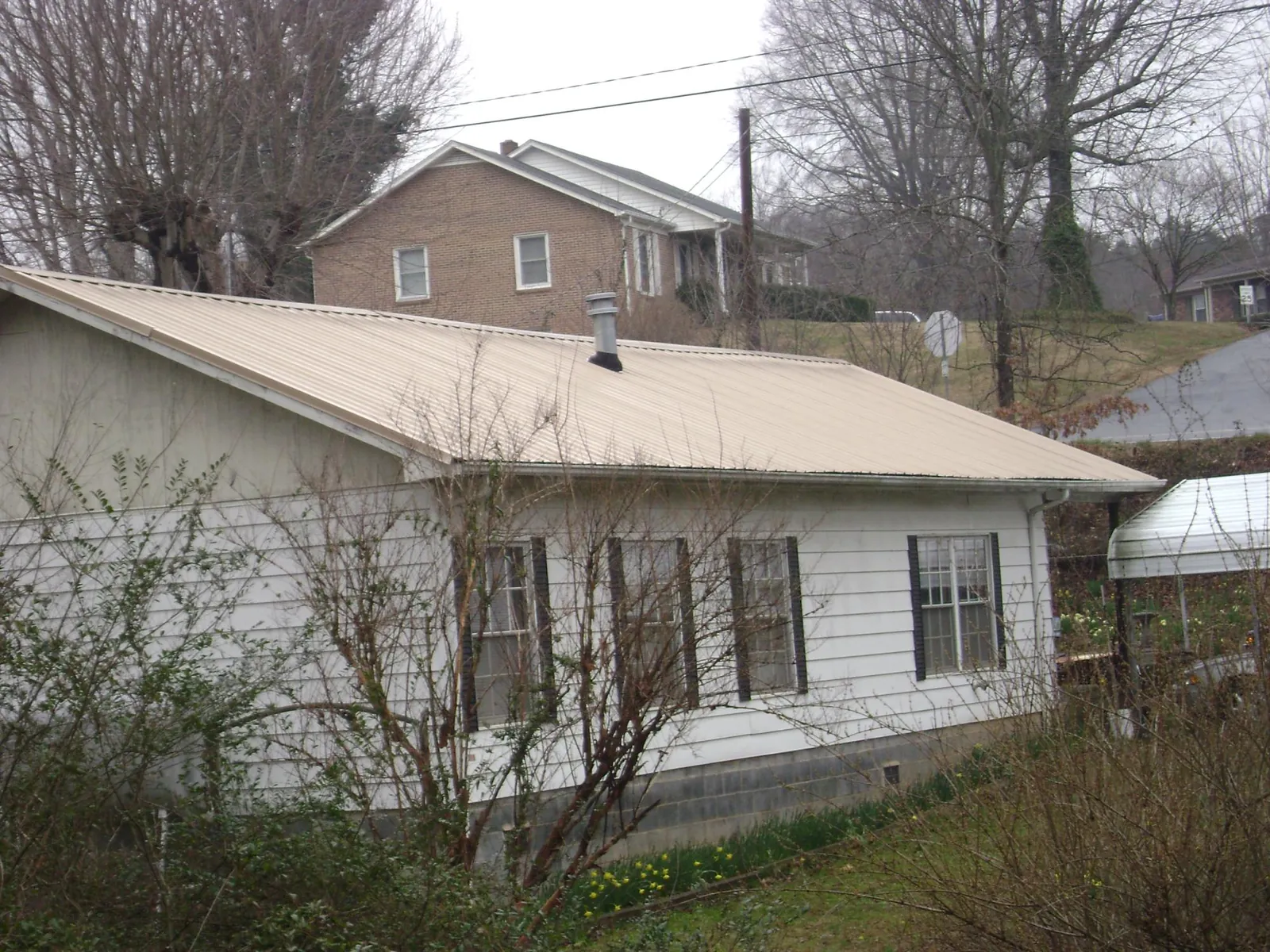 Tan metal roof on a white sided house set into a hillside — Commercial Roofing by Roofing Brothers in Bedford